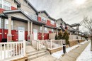 The property features a row of multi-level townhomes with red and grey siding, white doors, and front porches - 86 4029 Orchards Drive, Edmonton, AB  - Outdoor With Facade 