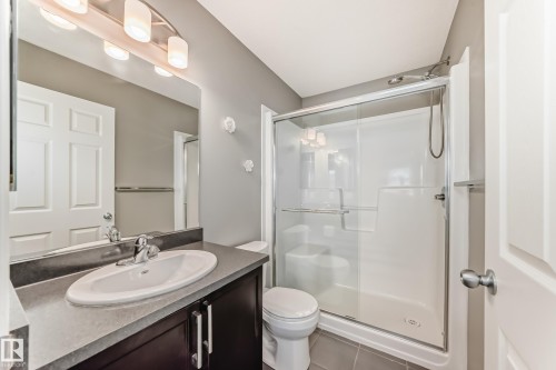 The bathroom features a vanity with a sink, a mirror with overhead lighting, a toilet, and a glass-enclosed shower - 86 4029 Orchards Drive, Edmonton, AB - Indoor Photo Showing Bathroom