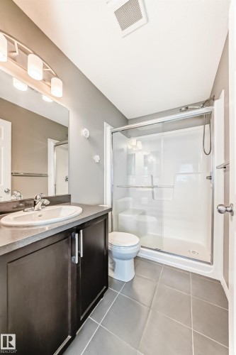 Bathroom featuring a dark wood vanity with a white basin sink, a mirrored wall, and a shower with a glass enclosure - 86 4029 Orchards Drive, Edmonton, AB - Indoor Photo Showing Bathroom