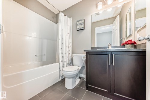 The bathroom features a white bathtub, a toilet, a vanity with a dark wood cabinet, and a large mirror with overhead lighting - 86 4029 Orchards Drive, Edmonton, AB - Indoor Photo Showing Bathroom