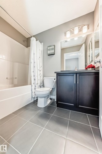 Bathroom featuring a white bathtub with a shower curtain, a white toilet, and a dark wood vanity with a countertop and a mirror - 86 4029 Orchards Drive, Edmonton, AB - Indoor Photo Showing Bathroom
