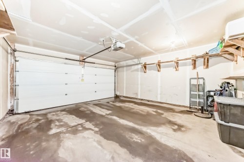 Spacious garage featuring a large overhead door, an automatic garage door opener, and integrated wall shelving for storage - 86 4029 Orchards Drive, Edmonton, AB - Indoor Photo Showing Garage