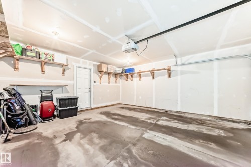 Spacious garage featuring concrete flooring, built-in shelving for storage, and an overhead garage door opener - 86 4029 Orchards Drive, Edmonton, AB - Indoor Photo Showing Garage