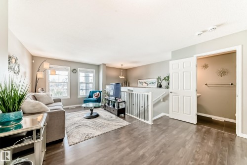 The living area features wood-style flooring, a light-colored area rug, and two windows providing natural light - 86 4029 Orchards Drive, Edmonton, AB - Indoor