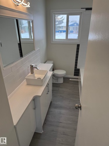 Bathroom featuring a white vanity with a rectangular vessel sink, a toilet, a window, and vinyl plank flooring - 13323 68 Street, Edmonton, AB - Indoor Photo Showing Bathroom
