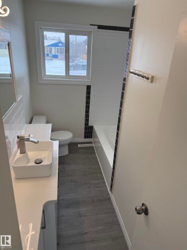 Bathroom featuring a modern vessel sink, white vanity countertop, white subway tile accents, and gray vinyl plank flooring - 13323 68 Street, Edmonton, AB - Indoor Photo Showing Bathroom