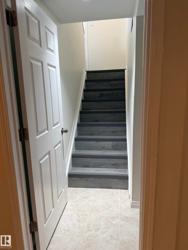 Staircase featuring luxury vinyl planks, white risers, and a tiled floor at the base - 13323 68 Street, Edmonton, AB - Indoor Photo Showing Other Room