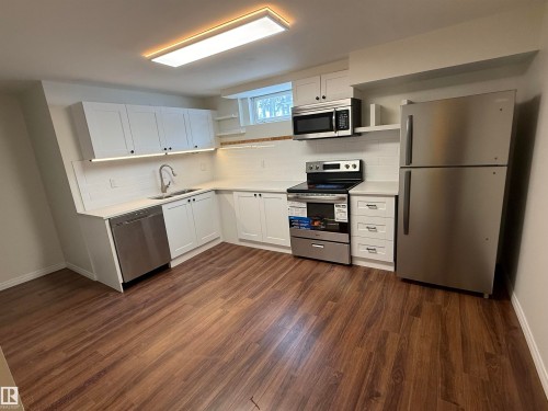 Kitchen featuring white cabinetry, stainless steel appliances, a white tile backsplash, and wood-look flooring - 13323 68 Street, Edmonton, AB - Indoor Photo Showing Kitchen With Double Sink