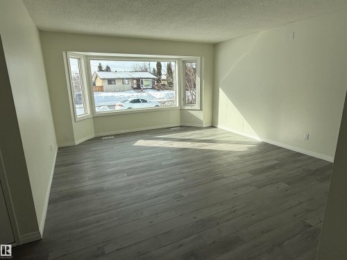 This room features a large bay window, light-colored walls, and luxury vinyl plank flooring - 13323 68 Street, Edmonton, AB - Indoor Photo Showing Other Room
