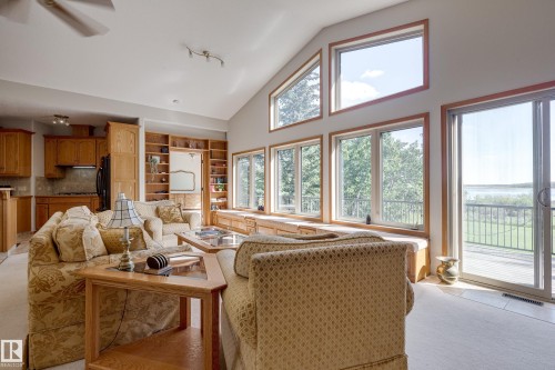 The open-concept living area features a vaulted ceiling, extensive built-in shelving, and large windows with views of the surrounding trees and water - 602 Pheasant Close, Rural Camrose County, AB - Indoor