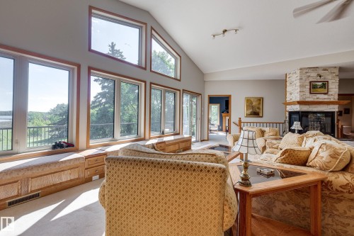 The living space features a vaulted ceiling, large windows providing expansive views, and a stone fireplace with a wooden mantel - 602 Pheasant Close, Rural Camrose County, AB - Indoor Photo Showing Living Room