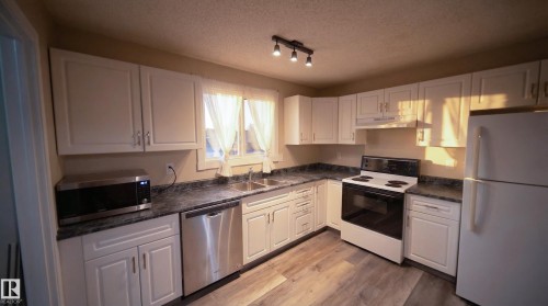 Kitchen featuring stainless steel appliances, white cabinets, a textured ceiling, light wood finished floors, and under cabinet range hood - 2311 146 Avenue, Edmonton, AB - Indoor Photo Showing Kitchen With Double Sink