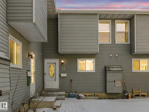The property features a grey horizontal siding exterior with white window frames and a white front door - 33 4403 Riverbend Road, Edmonton, AB - Outdoor