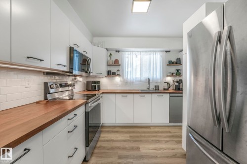 The kitchen features modern white cabinetry with dark hardware, butcher block countertops, and a subway tile backsplash - 33 4403 Riverbend Road, Edmonton, AB - Indoor Photo Showing Kitchen