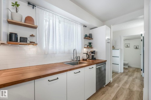 The kitchen features a stainless steel sink, white subway tile backsplash, wooden countertops, and white cabinetry with dark hardware - 33 4403 Riverbend Road, Edmonton, AB - Indoor Photo Showing Kitchen