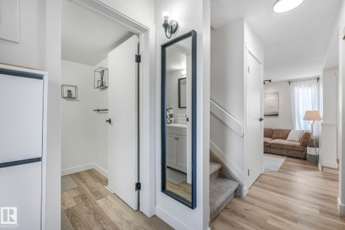 Welcoming entryway featuring light-toned flooring, a convenient built-in storage unit, and a mirror with a wall-mounted light fixture - 33 4403 Riverbend Road, Edmonton, AB - Indoor Photo Showing Other Room