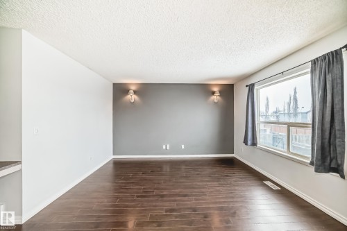 Spacious room featuring rich hardwood flooring, a contrasting accent wall with two sconce lights, and a large window with drapes - 1911 36 Avenue, Edmonton, AB - Indoor Photo Showing Other Room