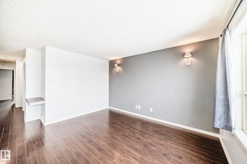Living room featuring dark hardwood floors, two wall sconces providing ambient lighting, and white baseboards - 1911 36 Avenue, Edmonton, AB - Indoor Photo Showing Other Room