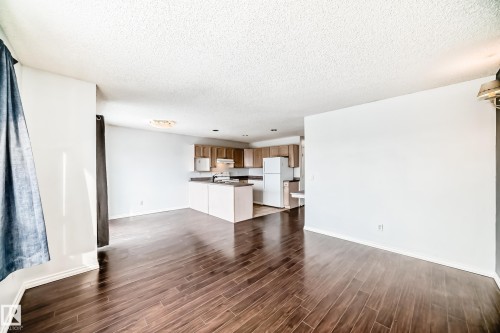 Spacious living area featuring dark wood flooring and white walls, with a kitchen visible in the background - 1911 36 Avenue, Edmonton, AB - Indoor Photo Showing Other Room