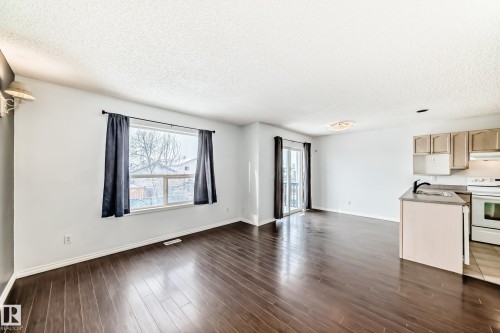 This open-concept area features dark wood flooring, a kitchen with light-colored cabinetry, a white stove, and a black faucet - 1911 36 Avenue, Edmonton, AB - Indoor Photo Showing Kitchen