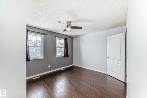 This room features rich hardwood flooring, two windows providing natural light, and a ceiling fan for climate control - 1911 36 Avenue, Edmonton, AB - Indoor Photo Showing Other Room