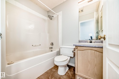 Bathroom featuring a white bathtub with a showerhead, a toilet, and a vanity with a sink and mirror - 1911 36 Avenue, Edmonton, AB - Indoor Photo Showing Bathroom