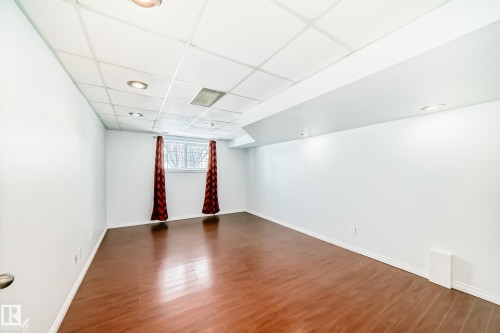 This room features warm-toned hardwood flooring, white painted walls, and a drop ceiling with recessed lighting - 1911 36 Avenue, Edmonton, AB - Indoor Photo Showing Other Room
