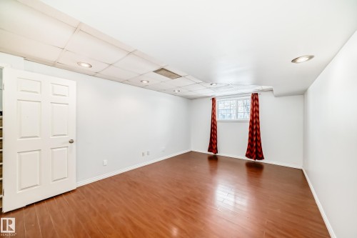 Spacious room featuring wood flooring, recessed lighting, and a window with red curtains - 1911 36 Avenue, Edmonton, AB - Indoor Photo Showing Other Room