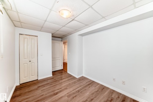 This interior space features wood-style flooring, a drop ceiling, and a light fixture providing illumination - 1911 36 Avenue, Edmonton, AB - Indoor Photo Showing Other Room