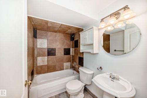 Bathroom featuring a white pedestal sink, a tiled shower and bath combination, a white storage cabinet, and an oval mirror - 1911 36 Avenue, Edmonton, AB - Indoor Photo Showing Bathroom