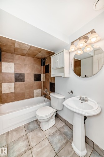 This bathroom features a white pedestal sink, a toilet, and a bathtub with a shower - 1911 36 Avenue, Edmonton, AB - Indoor Photo Showing Bathroom