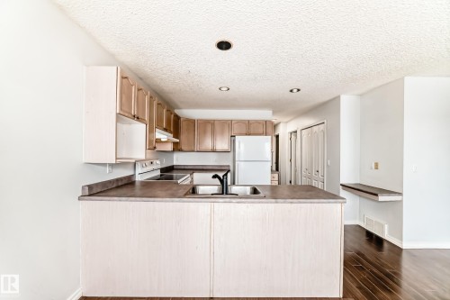 The kitchen features light wood cabinetry, a white refrigerator, and a dark countertop - 1911 36 Avenue, Edmonton, AB - Indoor Photo Showing Kitchen