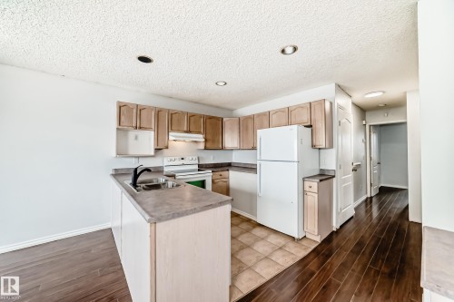 The kitchen features wooden cabinetry, a white refrigerator, and a white stove - 1911 36 Avenue, Edmonton, AB - Indoor Photo Showing Kitchen With Double Sink