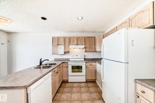 The kitchen features wood cabinetry, a double basin sink, and white appliances including a refrigerator, oven, and dishwasher - 1911 36 Avenue, Edmonton, AB - Indoor Photo Showing Kitchen With Double Sink