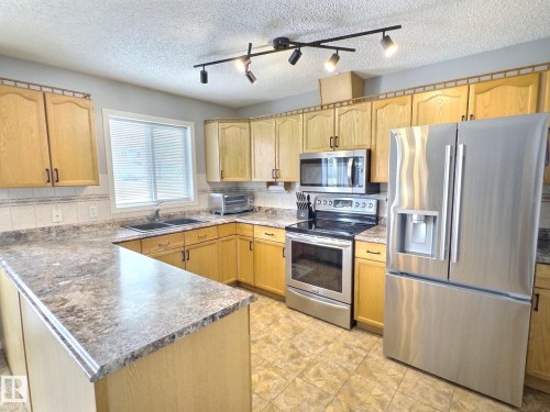 The kitchen features light wood cabinetry, stone-look countertops, stainless steel appliances, and track lighting - 14 6608 158 Avenue, Edmonton, AB - Indoor Photo Showing Kitchen With Double Sink