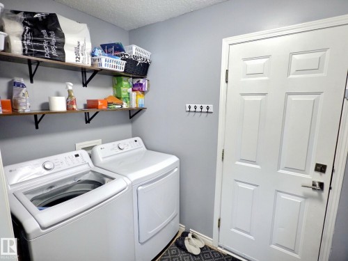Dedicated utility area featuring a washer and dryer, wall-mounted shelving for storage, and a white paneled door - 14 6608 158 Avenue, Edmonton, AB - Indoor Photo Showing Laundry Room