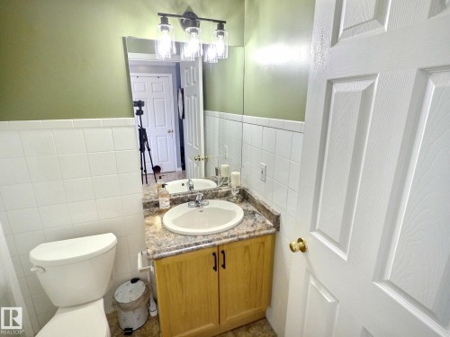 The bathroom features a vanity with a light-colored countertop and a white sink, set against a wall with white tile wainscoting - 14 6608 158 Avenue, Edmonton, AB - Indoor Photo Showing Bathroom