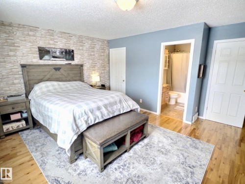 Bedroom featuring hardwood flooring, a textured accent wall, and a view into an en-suite bathroom with a shower - 14 6608 158 Avenue, Edmonton, AB - Indoor Photo Showing Bedroom