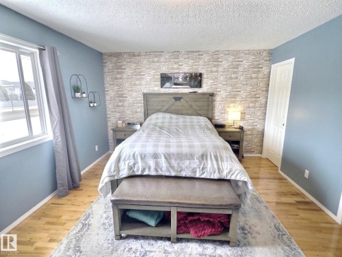This bedroom features light wood flooring, a window with curtains, and a decorative wall with a stone-like finish - 14 6608 158 Avenue, Edmonton, AB - Indoor Photo Showing Bedroom