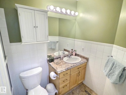Bathroom featuring a light wood vanity with a granite countertop and an integrated sink, a large mirror, and a wall-mounted light fixture with five bulbs - 14 6608 158 Avenue, Edmonton, AB - Indoor Photo Showing Bathroom