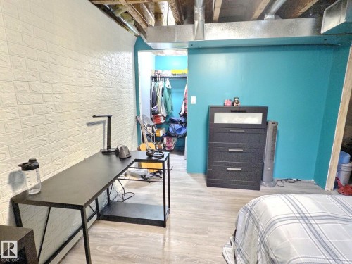 The property features exposed ceiling joists and ductwork, light-colored plank flooring, a wall with white brick-patterned paneling, and a vibrant turquoise accent wall - 14 6608 158 Avenue, Edmonton, AB - Indoor