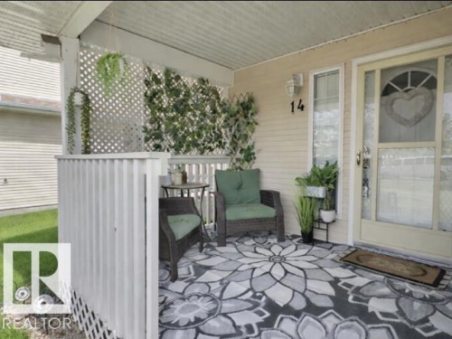 Inviting covered porch with a patterned rug, a privacy lattice, and a decorative front door with a heart-shaped window - 14 6608 158 Avenue, Edmonton, AB - Outdoor With Deck Patio Veranda With Exterior