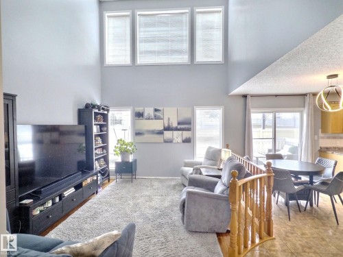 The living area features a high ceiling with three upper windows, a sliding glass door providing outdoor access, and a wood banister - 14 6608 158 Avenue, Edmonton, AB - Indoor Photo Showing Living Room