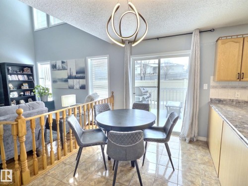 This bright dining area features tiled flooring, a modern chandelier, and sliding glass doors leading to an outdoor deck - 14 6608 158 Avenue, Edmonton, AB - Indoor Photo Showing Dining Room