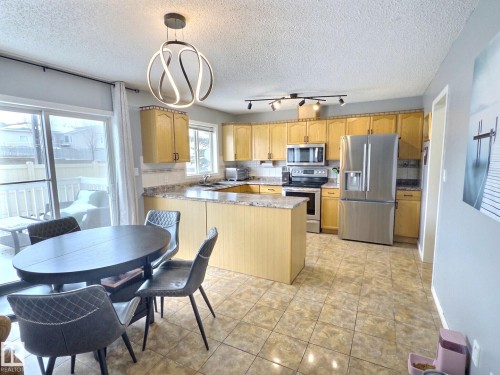 The kitchen features wood cabinetry, stainless steel appliances, and a tiled floor - 14 6608 158 Avenue, Edmonton, AB - Indoor