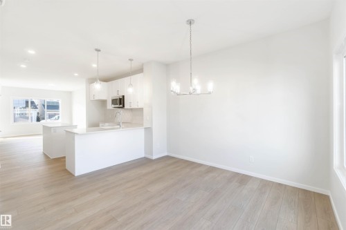 Open-concept kitchen and dining area featuring light wood flooring, white cabinetry, a kitchen island, and a modern chandelier - 18940 28 Avenue, Edmonton, AB - Indoor Photo Showing Kitchen