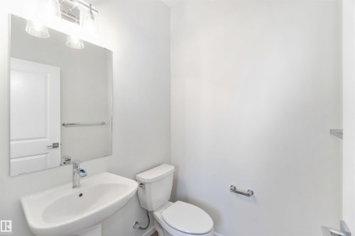 Powder room featuring a pedestal sink, a toilet, a mirror, and a wall-mounted light fixture - 18940 28 Avenue, Edmonton, AB - Indoor Photo Showing Bathroom
