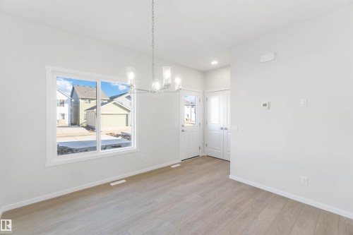 This inviting space features a large window, light-colored flooring, and a modern chandelier, creating a bright and open atmosphere - 18940 28 Avenue, Edmonton, AB - Indoor Photo Showing Other Room