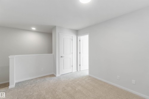 This inviting space features light-colored carpeting, white walls, and a white interior door with a silver handle - 18940 28 Avenue, Edmonton, AB - Indoor Photo Showing Other Room