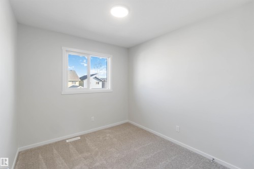 This room features light-colored walls, carpeted flooring, and a window providing natural light and exterior views - 18940 28 Avenue, Edmonton, AB - Indoor Photo Showing Other Room
